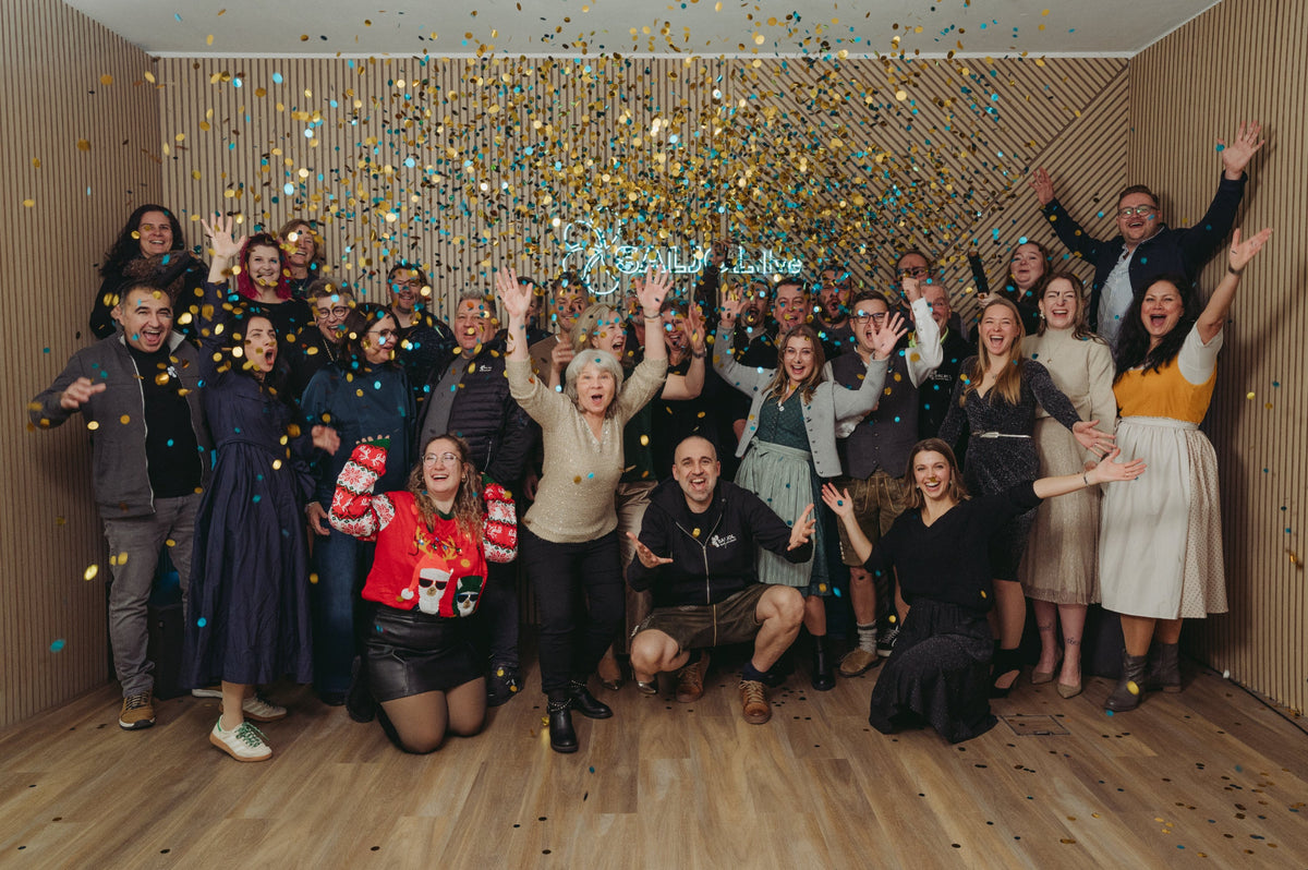 Das gesamte Saljol-Team feiernd auf einem Gruppenbild mit Konfettiregen aus Gold und Türkis