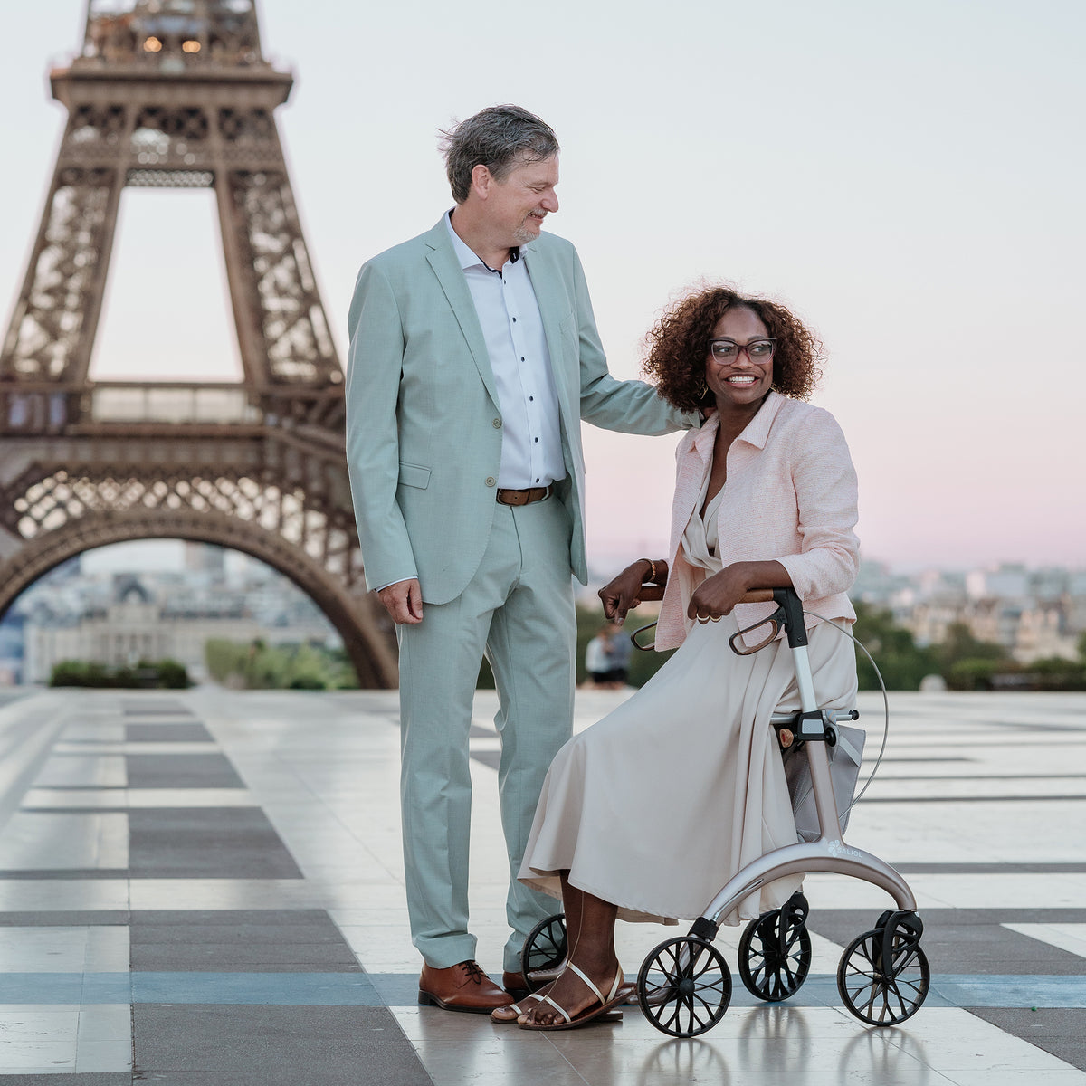 Sitzen auf dem Carbon Rollator Superlight Rose Gold vor dem Eiffelturm
